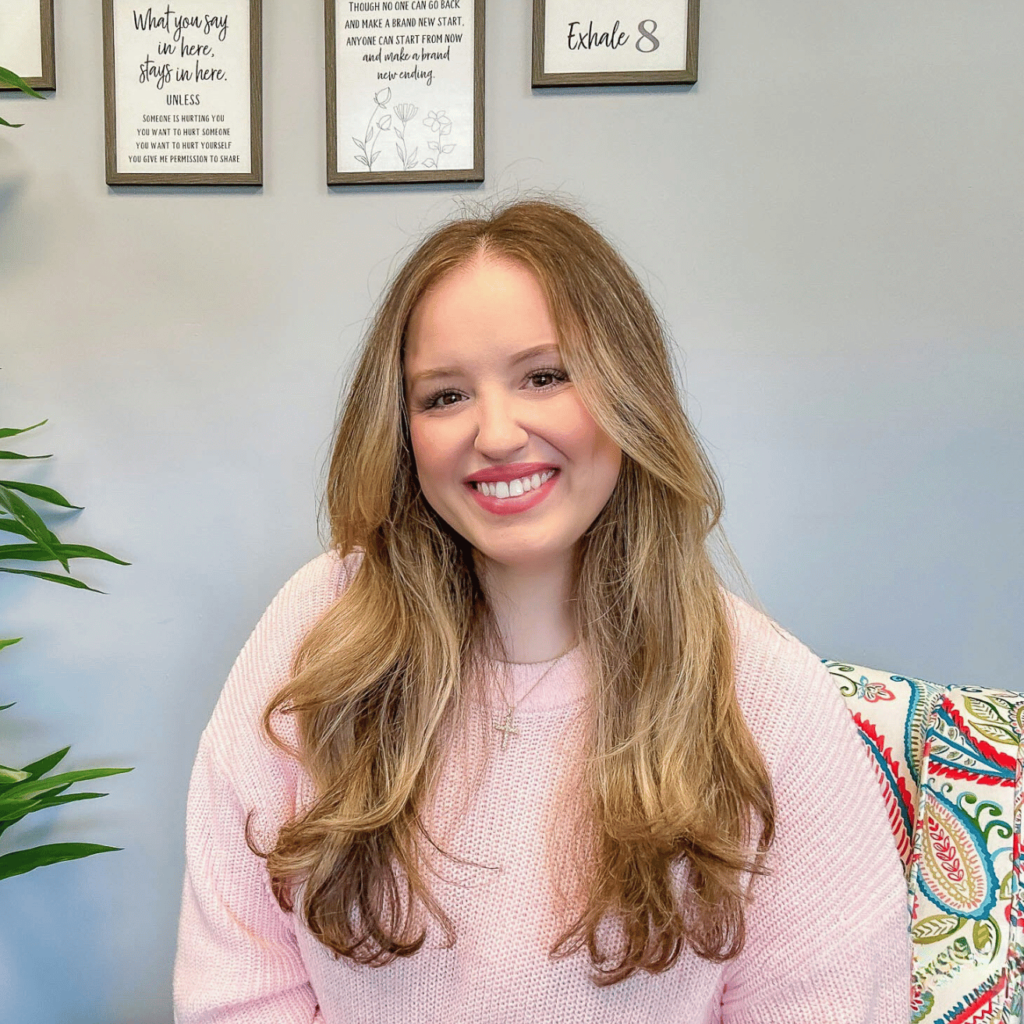 Image of Alexa Sadowsky, owner of Open Minded Marriage and Family Therapy, PLLC, wearing a soft pink sweater as she sits and smiles for the camera.