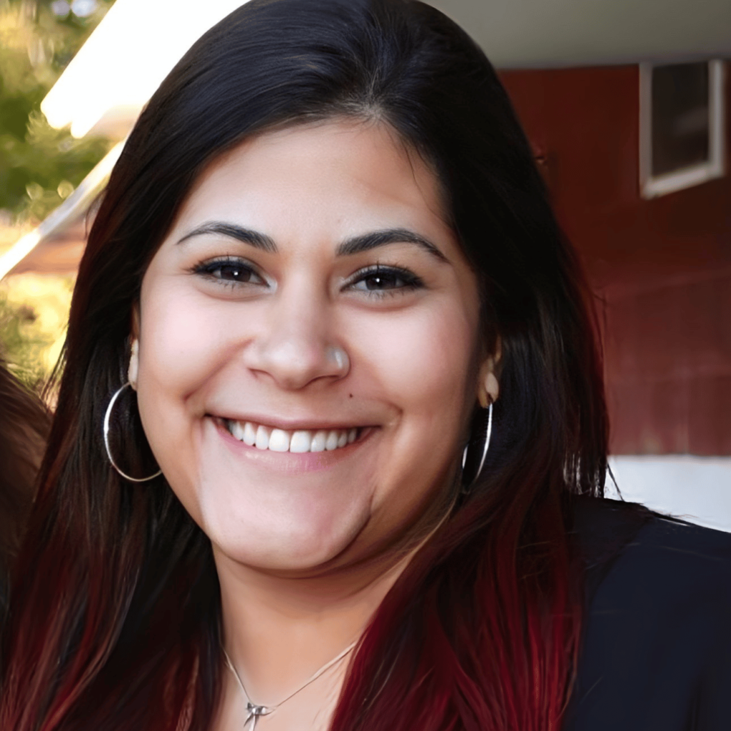 Image of Gabriela Giron with long straight black hair with red tips in a black top, smiling at the camera.