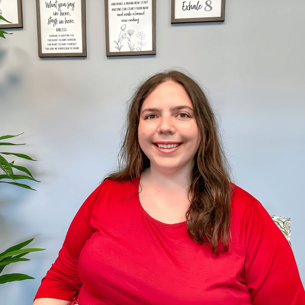 Image of Julie Wisher, LCSW with long brown hair and a red top, smiling at the camera against a gray background.