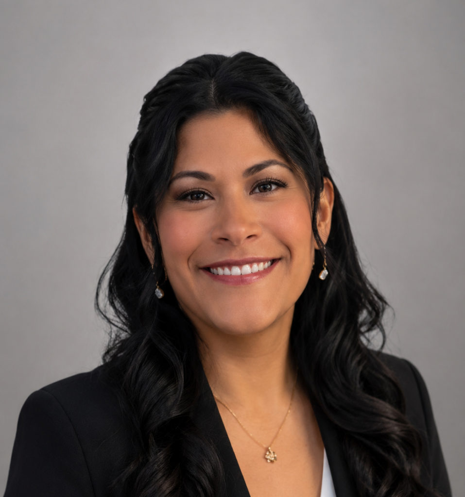 Image of Gabriela Giron, LCSW with long dark hair and a black blazer with white v-neck top, smiling at the camera against a gray background.